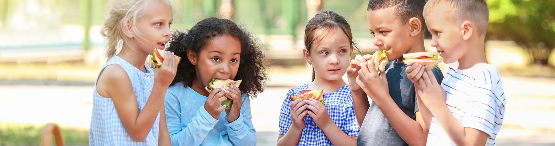 5 small children eating sandwiches outside